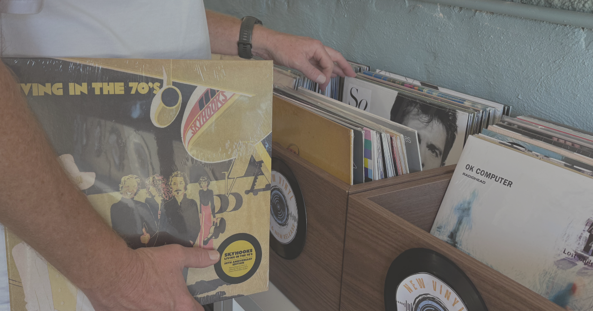 Hands holding Skyhooks Living in the 70's on vinyl beside tubs of new records at Peninsula Records & Books in Stansbury