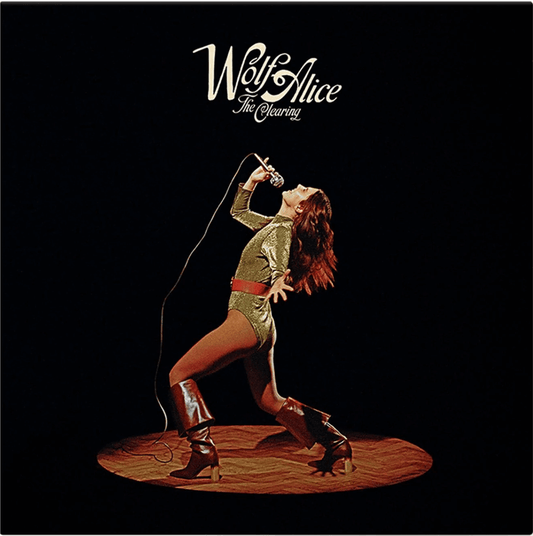 Album cover of The Clearing by Wolf Alice, featuring a retro-style photograph of a woman in a gold outfit and red boots singing into a microphone on stage under a spotlight, with the band’s name and album title in white script at the top.